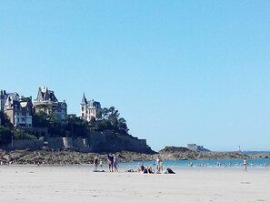 A beach with a large, historic building on a cliff.