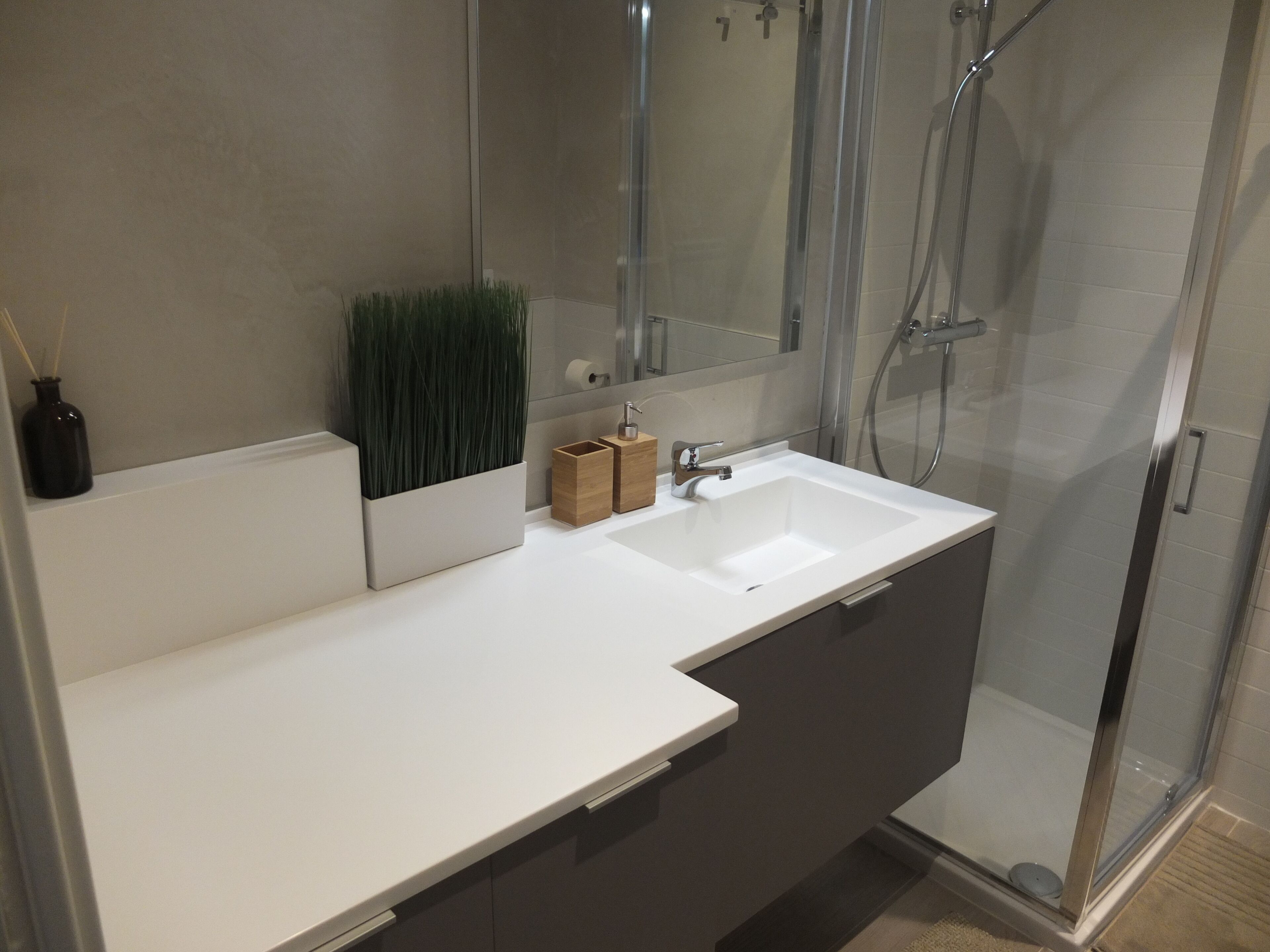 Un bany modern amb taulell blanc, una cabina de dutxa de vidre i un mirall sobre el lavabo.