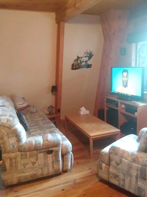 Un salon chaleureux avec un canapé, une table basse en bois et un téléviseur qui diffuse une émission mettant en scène une personne.