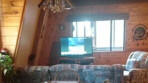 Ein gemütliches Blockhauss-Interieur mit Esstisch für vier Personen, einer Couch und einem Fernseher im Hintergrund.