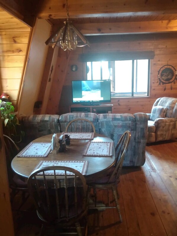 L’intérieur chaleureux d’un chalet avec une table à manger dressée pour quatre personnes, un canapé et un téléviseur en arrière-plan.