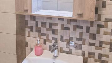 Une salle de bain avec un lavabo blanc, un miroir au-dessus et un mur recouvert de carreaux derrière le lavabo.
