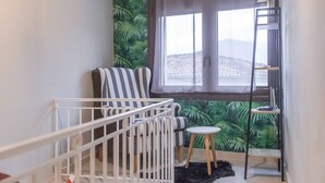 A room with a crib, a striped chair, a small table, a ladder, and a window with a curtain. - Historic Luxury House Heart of Meteora (Kalabaka)