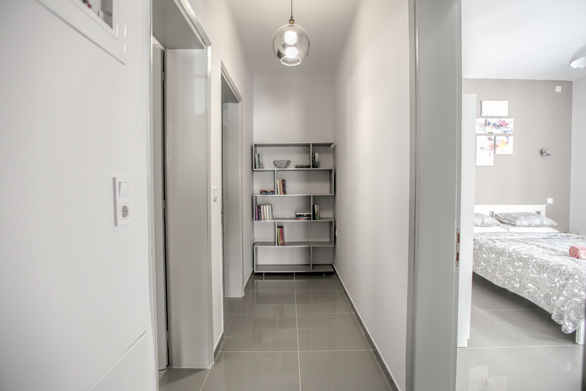 A narrow hallway leading to a bedroom with a bed and a shelf unit.