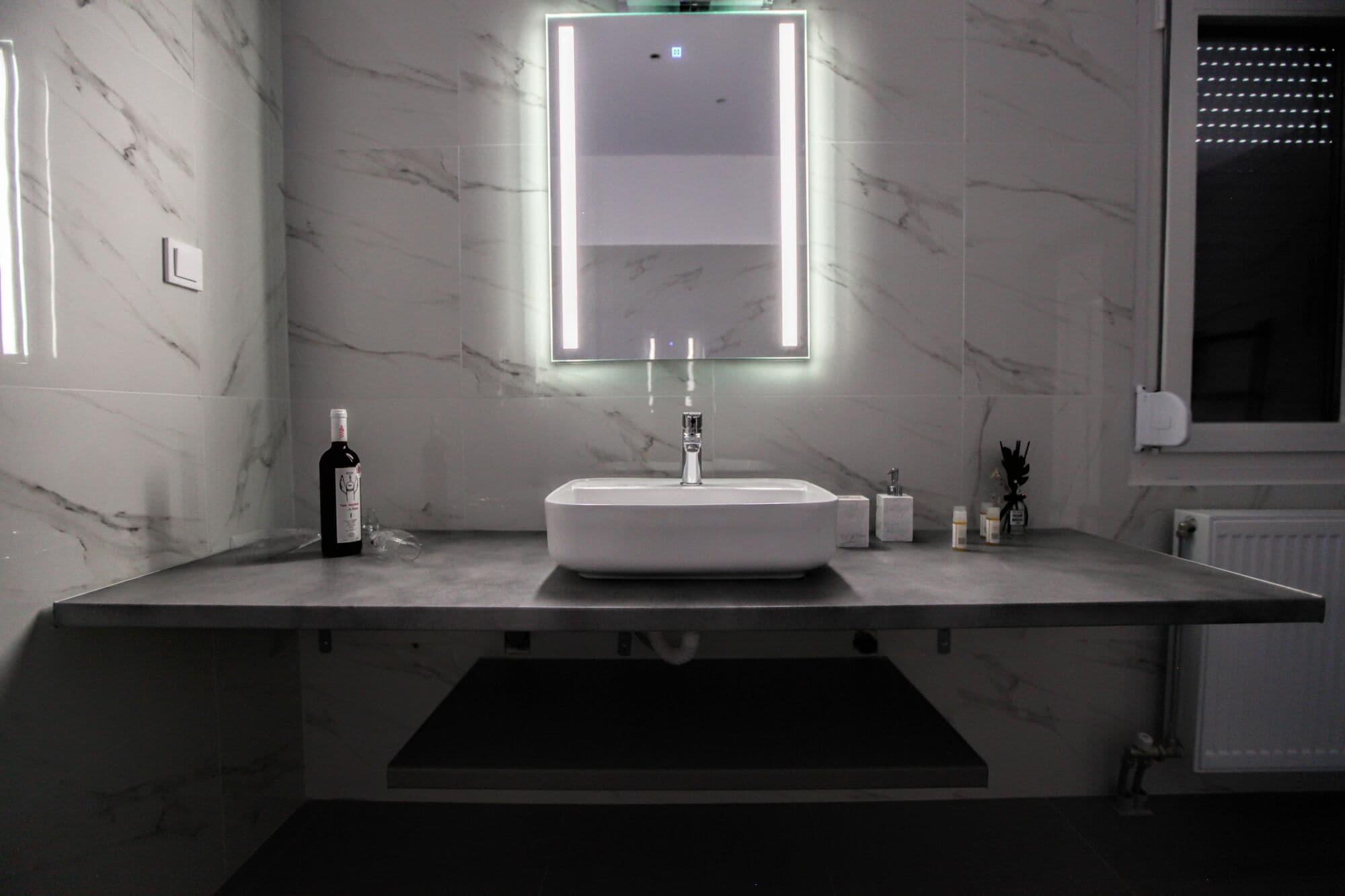 A modern bathroom with a marble countertop, a white sink, and a mirror with LED lighting.