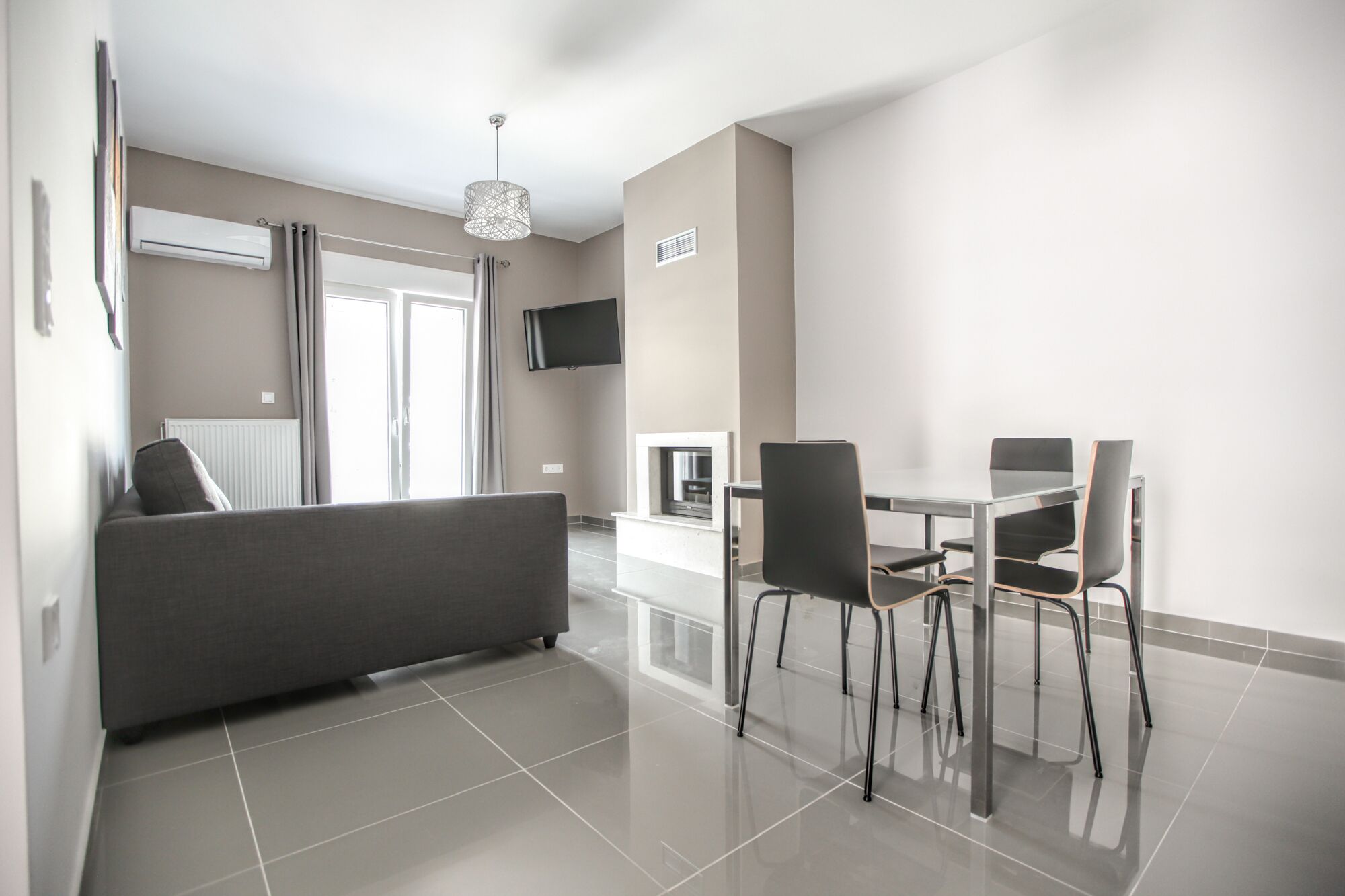 Een moderne woonkamer met een bank, een eettafel, stoelen en een aan de muur bevestigde televisie.