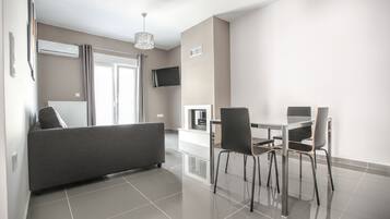 Een moderne woonkamer met een bank, een eettafel, stoelen en een aan de muur bevestigde televisie.