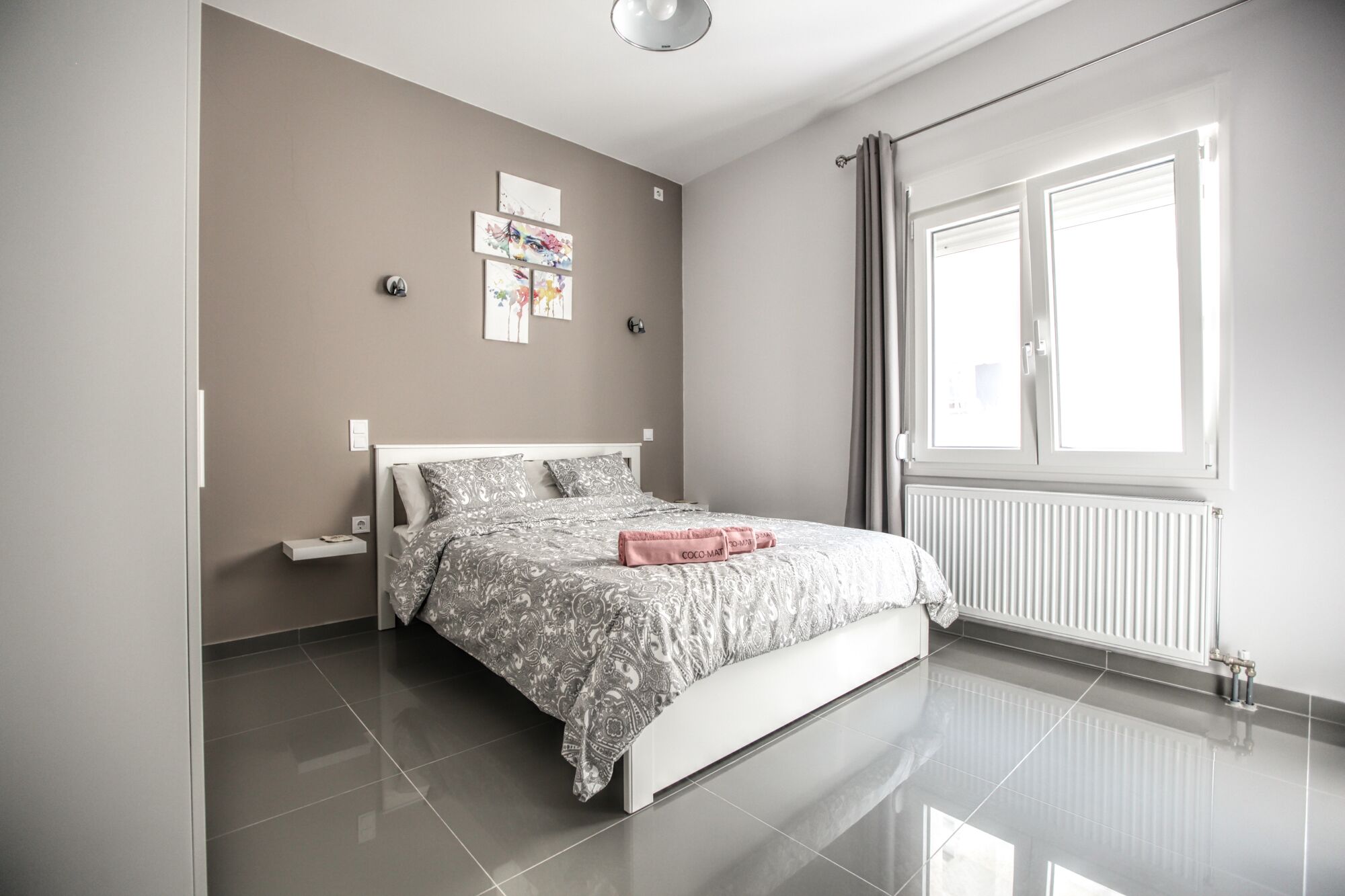 A modern bedroom with a bed, a nightstand, a window with curtains, and artwork on the wall.