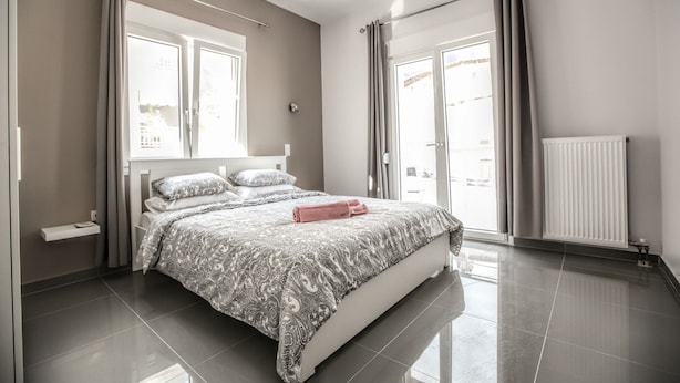 A modern bedroom with a large bed, a bedside table, a radiator, and a view of the outside through the window.