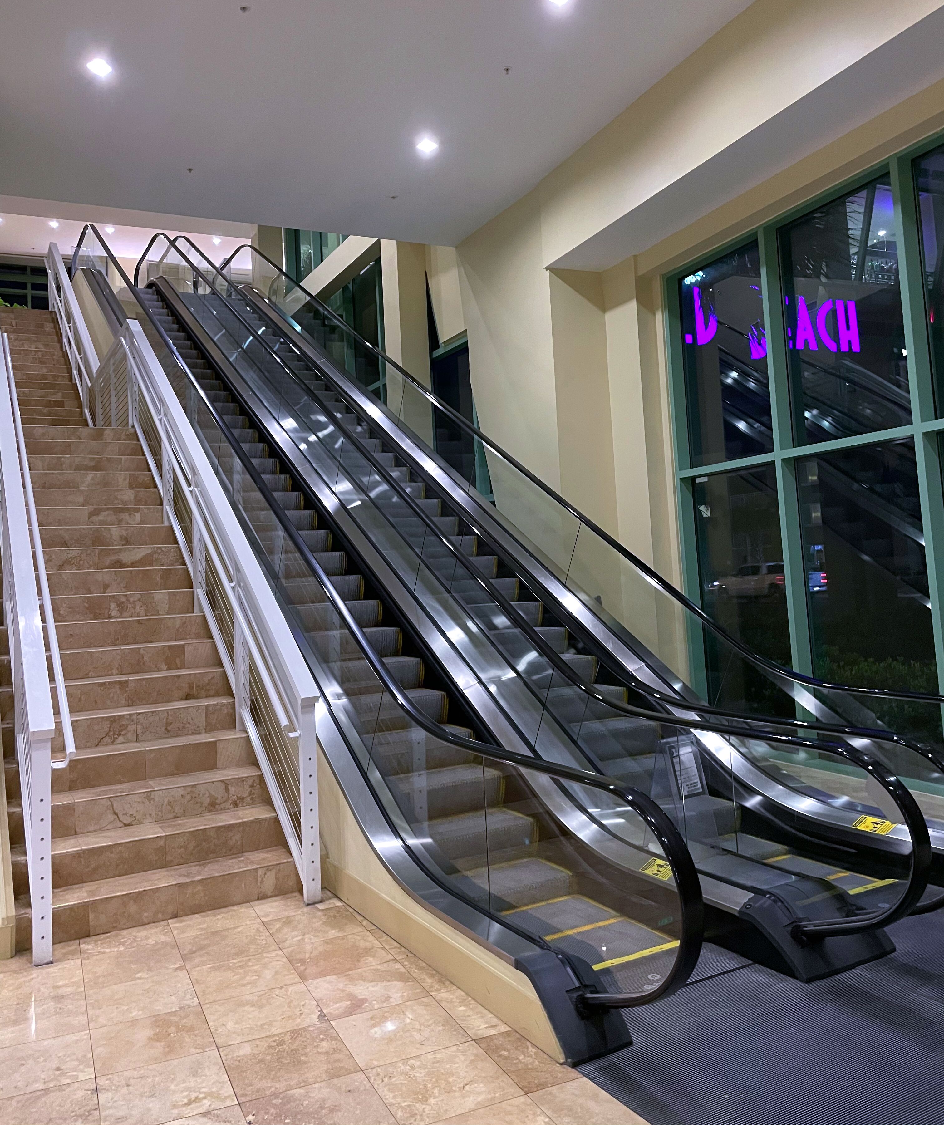 An indoor escalator adjacent to a staircase with a glass railing.