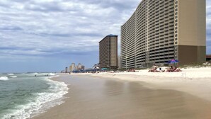 Un hotel frente a la playa con varios pisos, una playa de arena y un muelle al fondo.