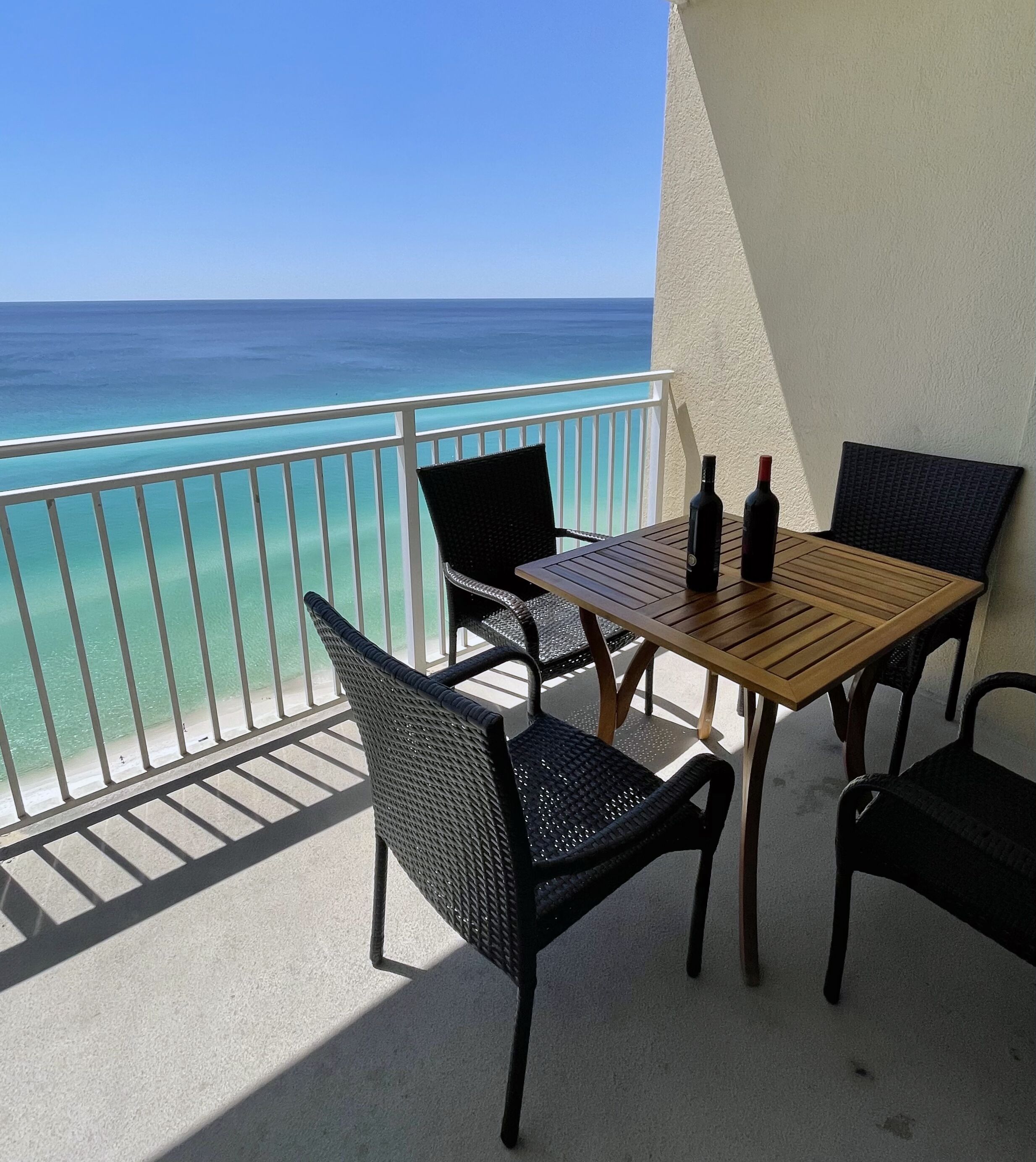 Un balcon avec une table en bois et quatre chaises, donnant sur une plage et l’océan.