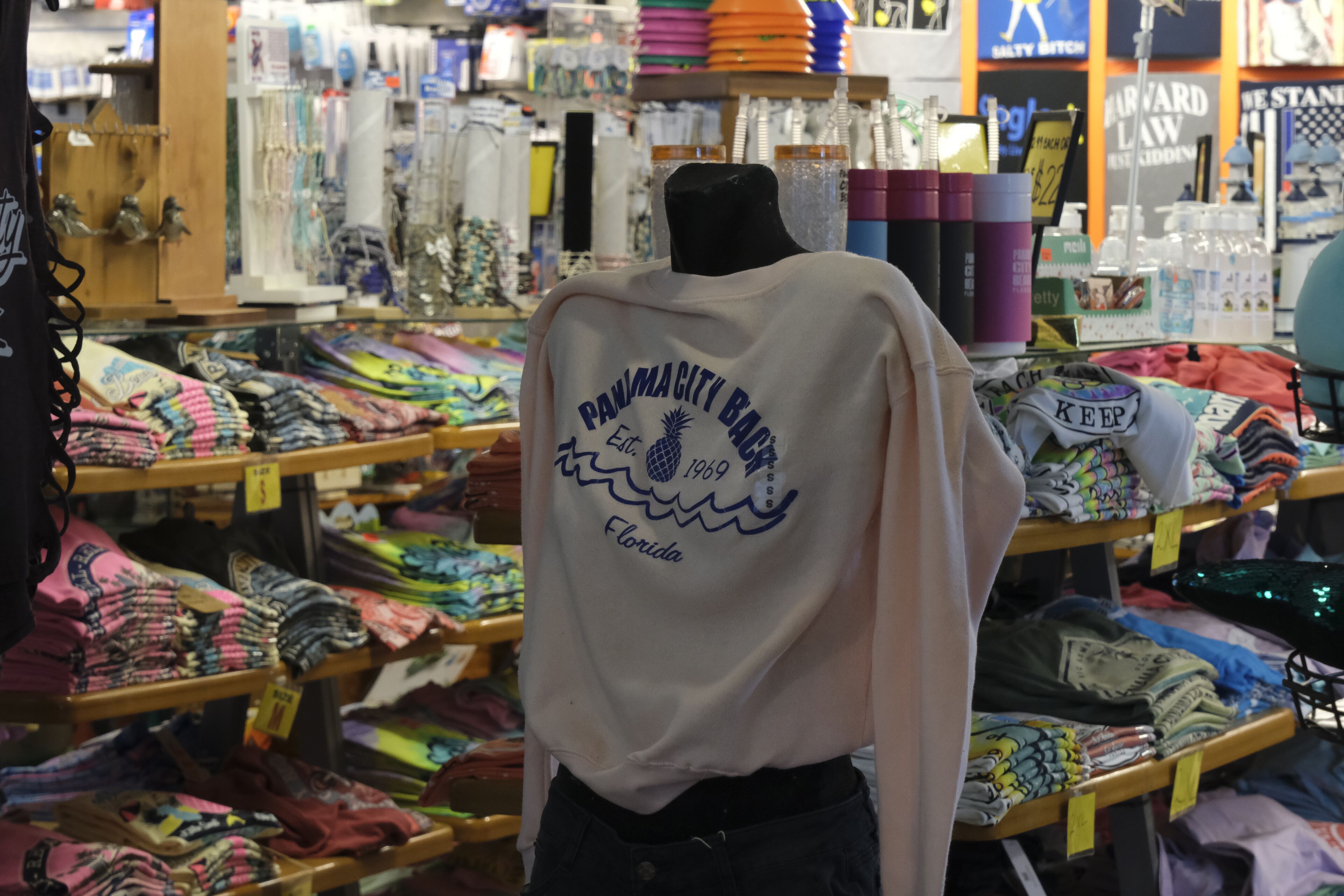 Negozio con scaffali pieni di vestiti piegati e un manichino che indossa una camicia bianca con scritte.