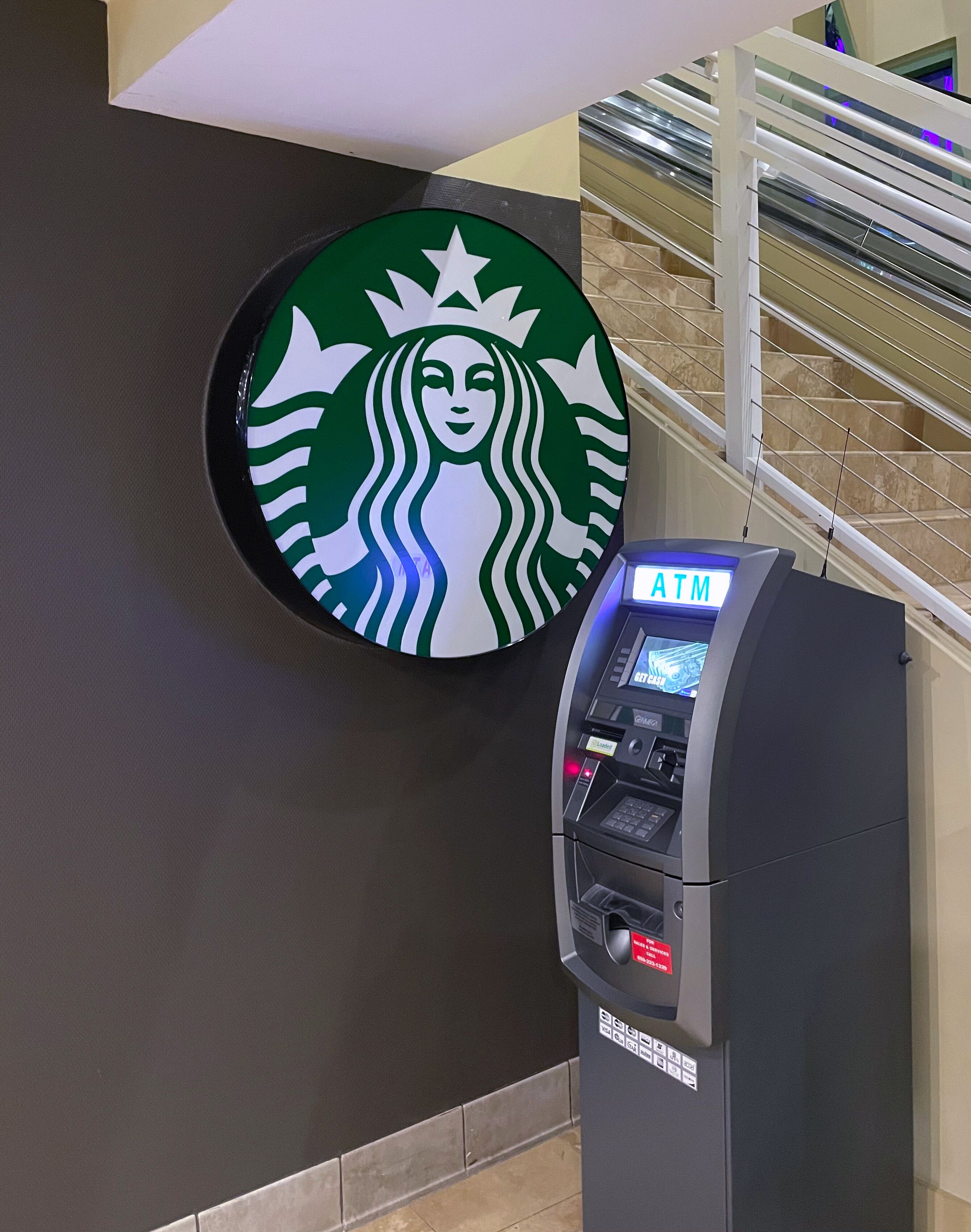 En Starbucks-logotyp och en bankomat i ett offentligt, inomhusutrymme.