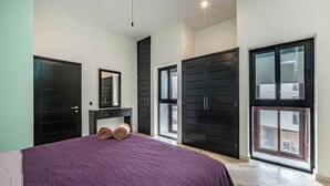 A bedroom with a large bed, a dresser, a mirror, and a window with a view. - Beautiful and comfortable apartment in a condominium facing the sea (Playa del Carmen)