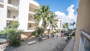 A multi-story building with balconies, palm trees, and a pedestrian walkway. - Beautiful and comfortable apartment in a condominium facing the sea (Playa del Carmen)