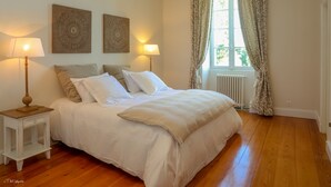 A neatly made bed with white linens and two lamps on nightstands, a window with curtains, and two wall art pieces. - DOMAINE DE CEZAC-Proche Bordeaux-St-Emilion-Arcachon-Blaye (Cezac)