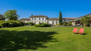 A large, historic building with a symmetrical facade, a well-maintained lawn, and two red signage boards. - DOMAINE DE CEZAC-Proche Bordeaux-St-Emilion-Arcachon-Blaye (Cezac)