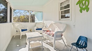 Une véranda couverte, aménagée avec des meubles en osier, une table et une chaise.