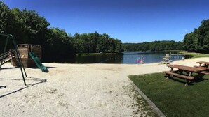 Zona de playa con arena, mesas de picnic y un parque infantil con tobogán.