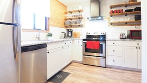 Una cocina moderna con electrodomésticos de acero inoxidable, estantes de madera y una encimera negra.