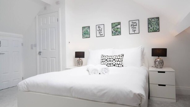Une chambre à coucher blanche, avec un lit, deux tables de chevet et quatre tableaux encadrés accrochés au mur.