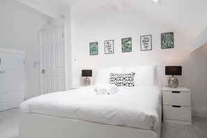 A white bedroom with a bed, two bedside tables, and four framed pictures on the wall.