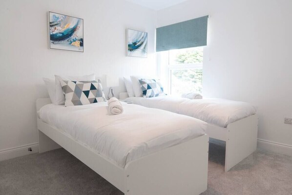 A bedroom with two single beds, white bedding, geometric patterned pillows, and abstract artwork on the walls.