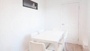 Une table à manger blanche avec quatre chaises, une porte blanche et un tableau encadré de noir accroché au mur.
