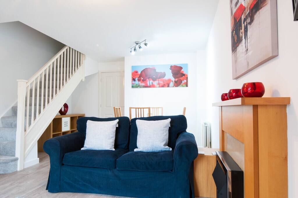 Un salon avec un canapé bleu foncé, des coussins blancs, une table basse en bois et un tableau représentant des fleurs rouges accroché au mur.