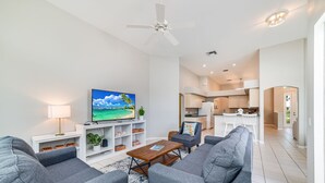 Ein modernes Wohnzimmer mit grauen Sofas, einem Couchtisch, einem Fernseher auf einem weißen Schrank und einem Deckenventilator.