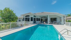 Ein Swimmingpool mit weißem Zaun, Liegestühlen und einer überdachten Terrasse.
