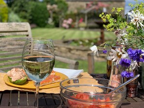 Une table avec un verre de vin blanc, une assiette de saumon fumé et du pain, un saladier de salade de tomates et un vase rempli de fleurs.