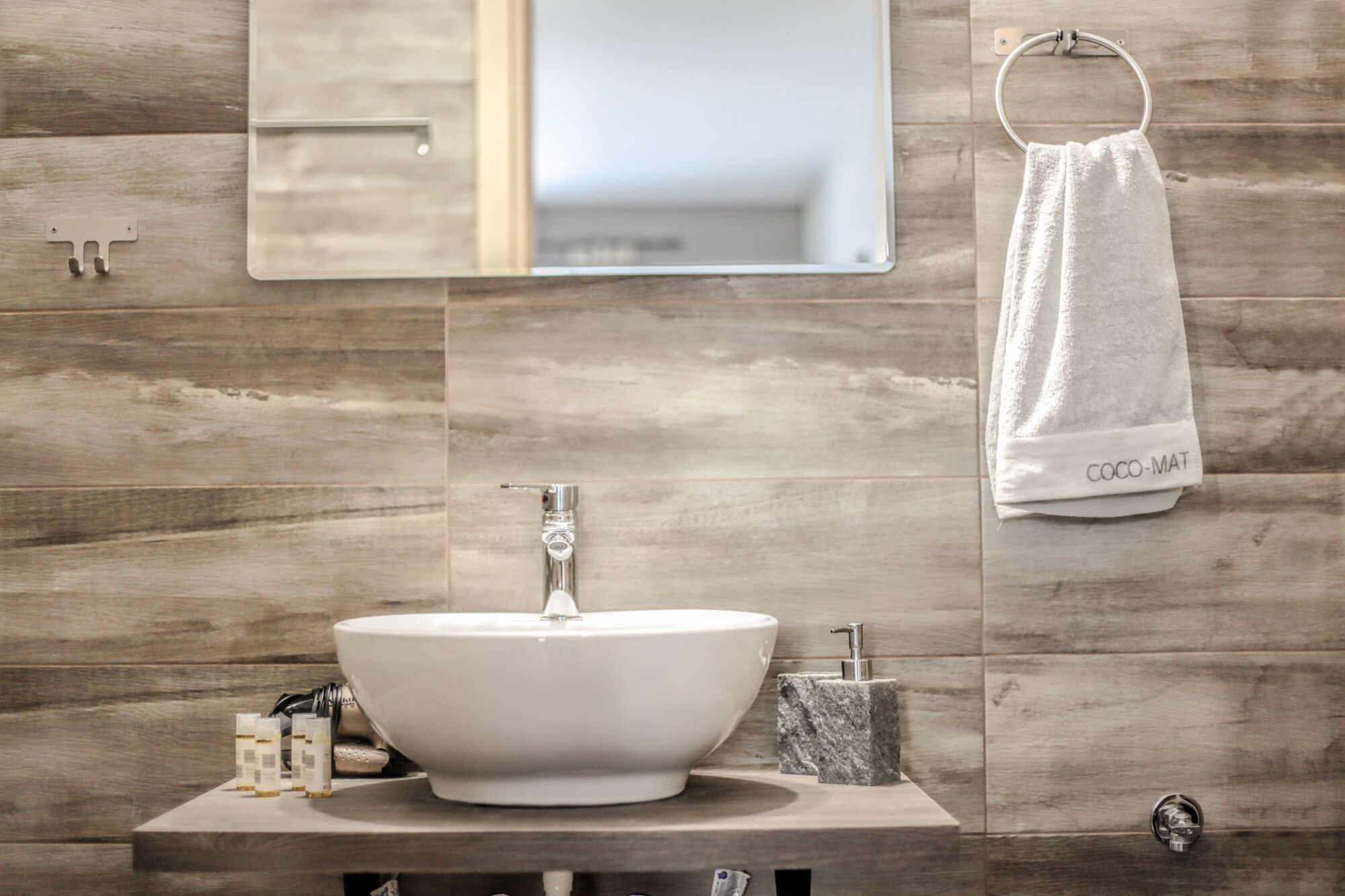 A bathroom with a wooden wall, a white sink, and a towel rack with a white towel labeled "COCO-MAT".