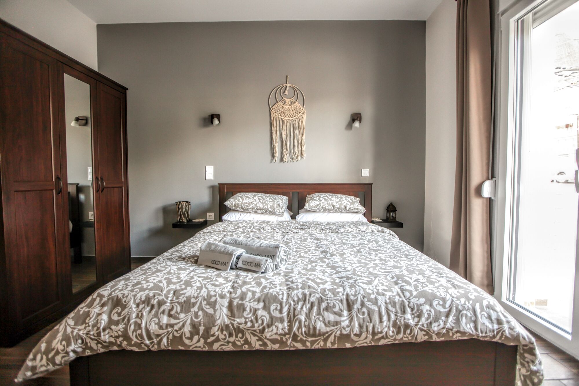 Een slaapkamer met een groot bed, een kledingkast, een macramé wanddecoratie en uitzicht op buiten.