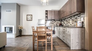 A modern kitchen with wooden cabinets, a tiled backsplash, and a dining area with a table and chairs. - Terra di Meteora Suites 2 (Kalabaka)