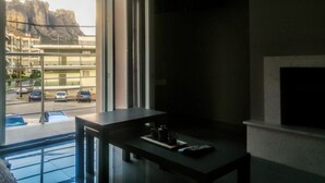 A room with a large window, a small table with a remote control, and a TV mounted on the wall. - Terra di Meteora Suites 2 (Kalabaka)