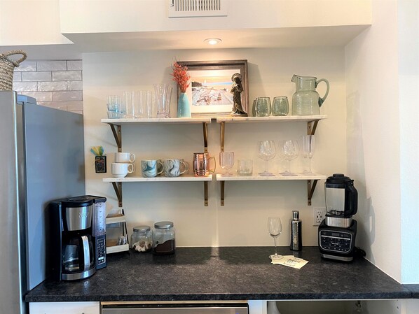 A kitchen with a refrigerator, coffee maker, and shelves with glassware and mugs. - Unobstructed Beach View End of Island - Private on Pensacola Beach (Pensacola Beach)