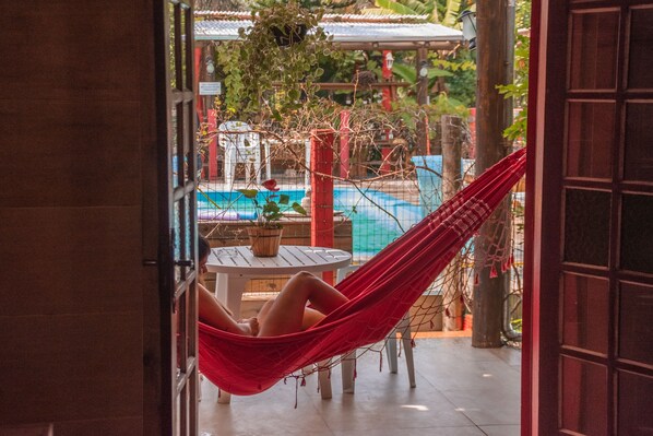 A hammock by a poolside, a wooden table with a potted plant, and a red door.