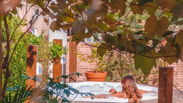 A hot tub in a wooden deck area surrounded by potted plants and a brick wall. - Hotel Ferrugem Eco Village (Garopaba)