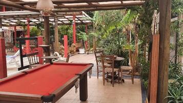 A pool table with a red felt surface, surrounded by wooden chairs and a small table.