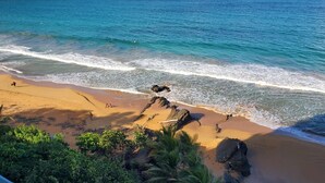 A beach with clear blue water, sandy shore, and some vegetation.