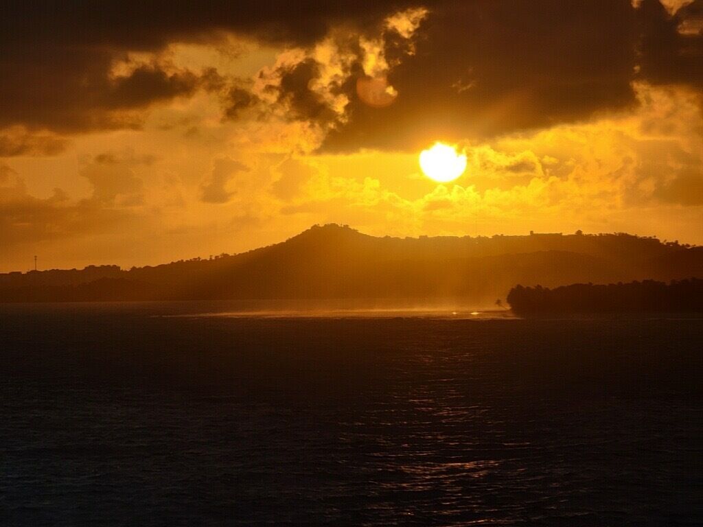 A sunset over a body of water with a silhouette of a hill in the distance.
