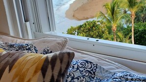 Una cama con almohadas estampadas y vistas a una playa con palmeras.