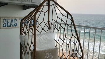 Una silla colgante de mimbre con cojines, un letrero que dice "SEAS TIDE" y vista al océano.