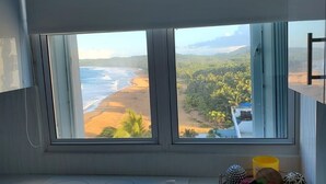 A kitchen with a large window overlooking a beach and greenery.