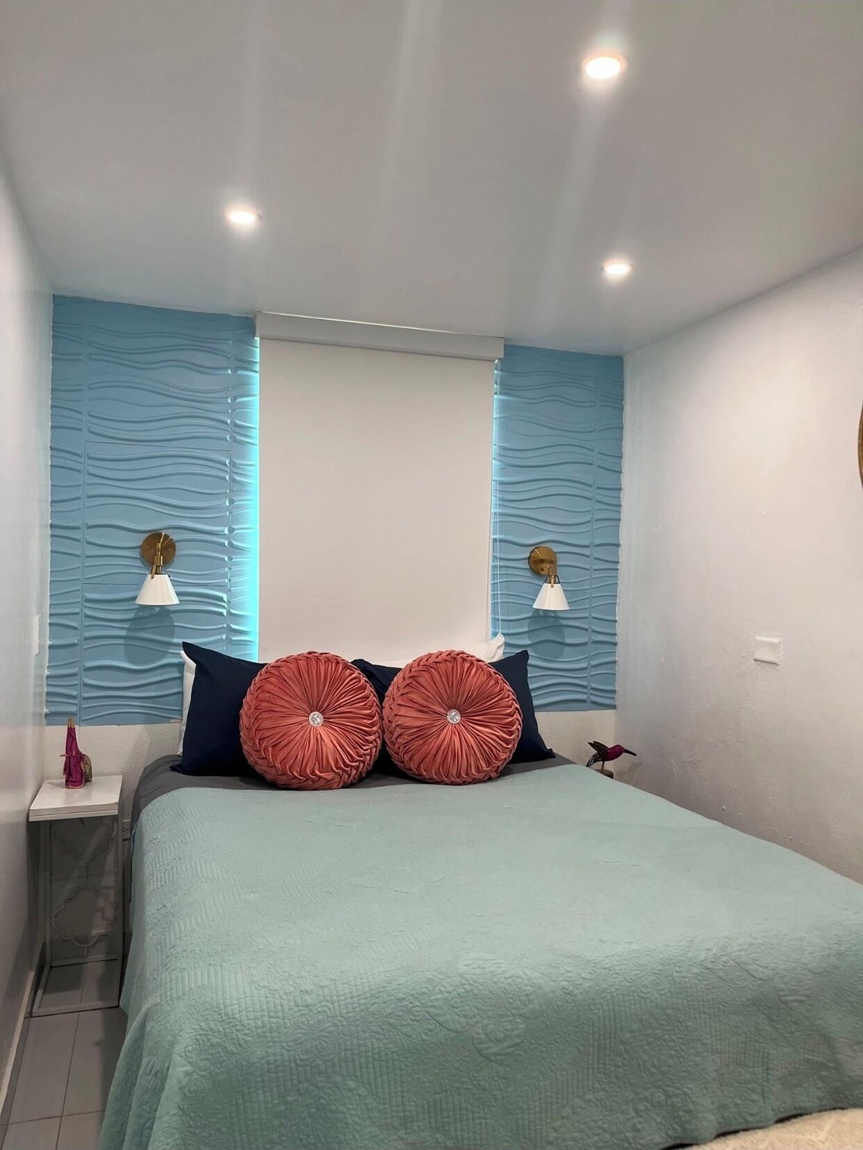 A bedroom with a bed, two wall-mounted lamps, and a window with curtains.