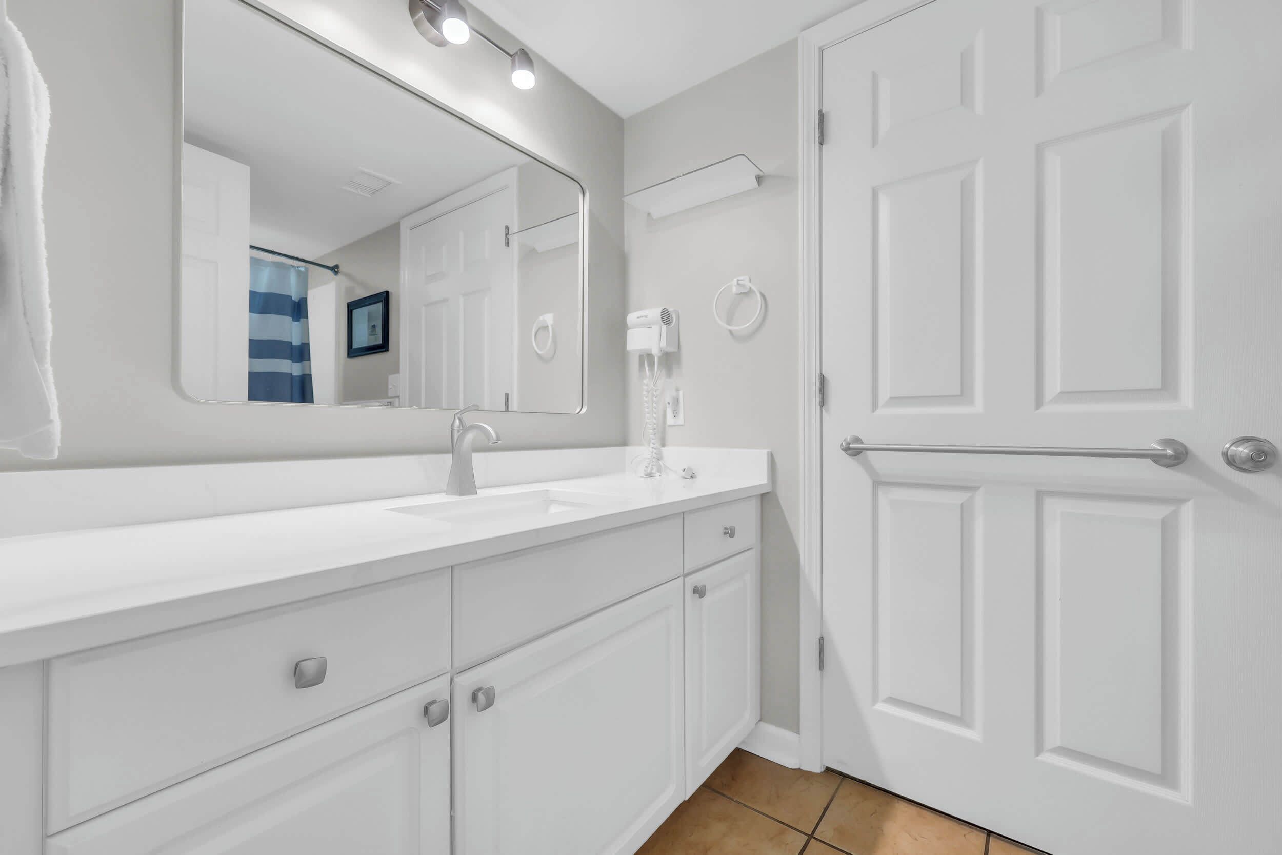 Un baño moderno con un tocador blanco, un espejo grande, un perchero y una puerta con barra para toallas.