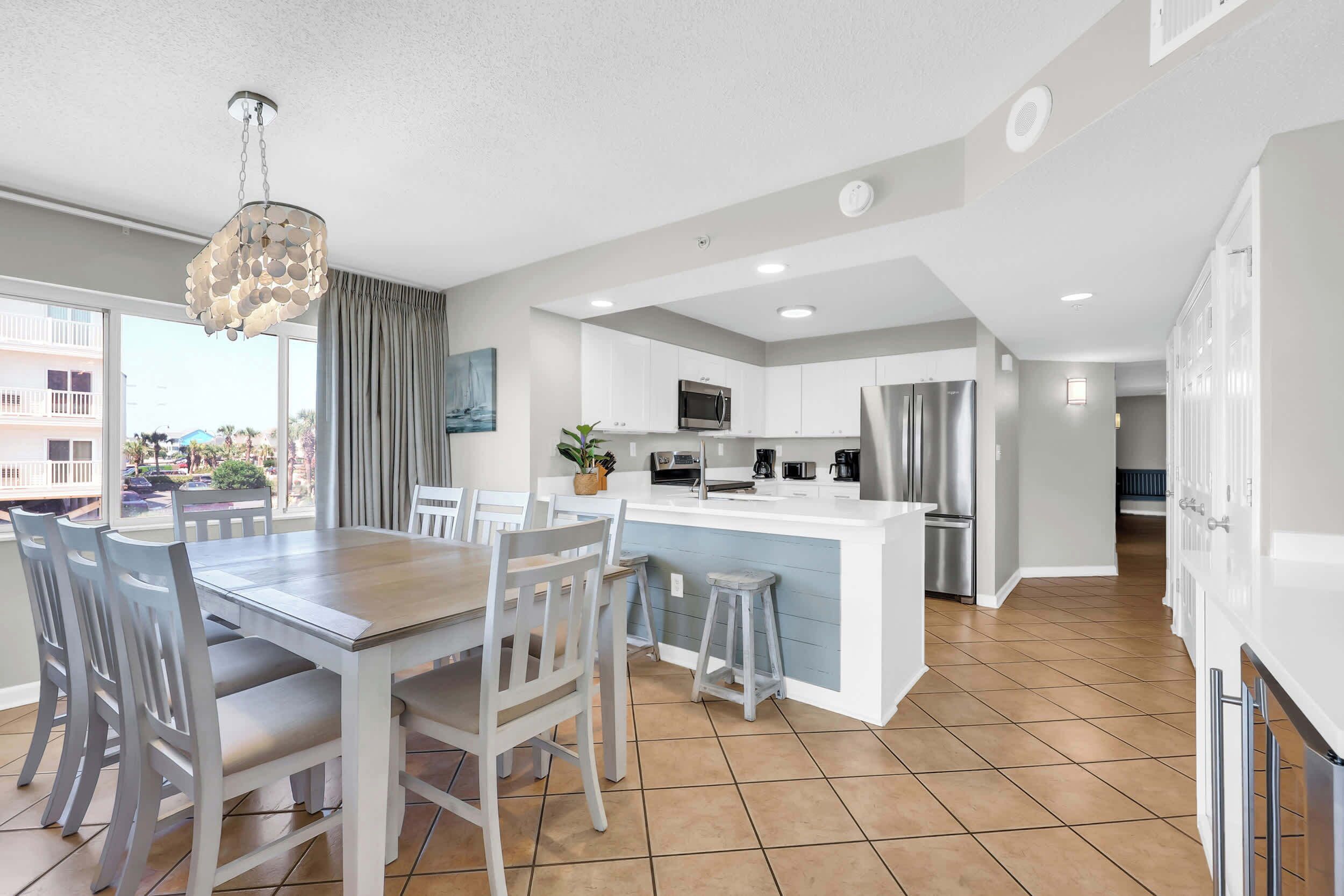 A modern kitchen with white cabinets, a central island, and a dining area with a wooden table and chairs.