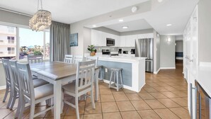 Una cocina moderna con armarios blancos, una isla central y una zona de comedor con mesa y sillas de madera.
